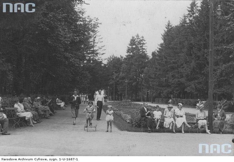 Fragment parku zdrojowego w Inowrocławiu - Fragment parku zdrojowego w Inowrocławiu, w którym wypoczywają spacerowicze. Widoczne dziecko na trójkołowym rowerze. Fotografia wykonana w latach 1918 - 1937.